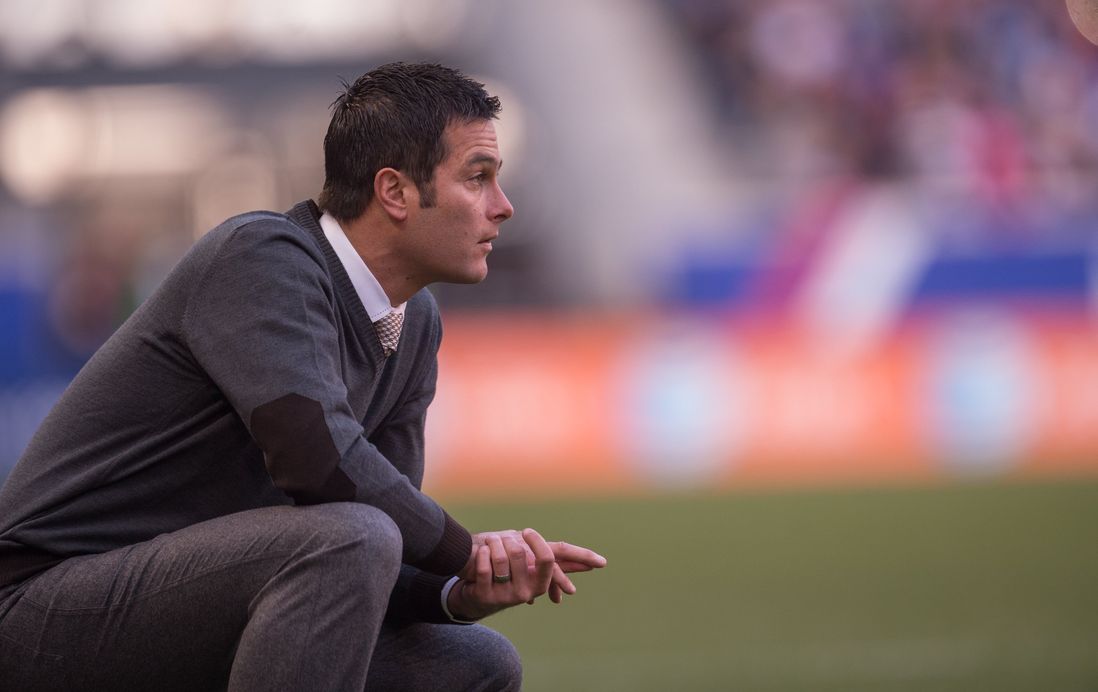 Mike Petke crouches on the sideline.